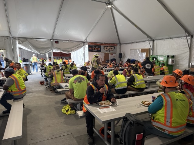 Construction crews sharing a catered meal at long tables under an event tent